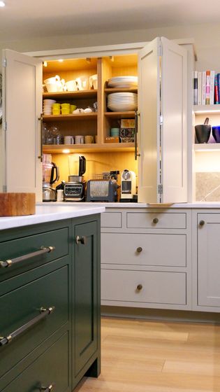 A Shaker kitchen featuring a green kitchen island, off white cabinets with open shelves displaying dishware, and various appliances like a coffee maker and blender.
