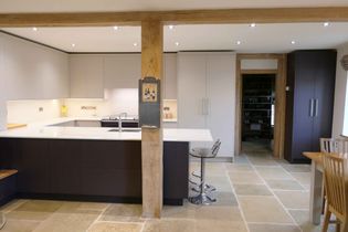 Modern kitchen featuring neutral tones, a central wooden beam, sleek countertops, bar stool, and recessed lighting, creating a warm and inviting space.