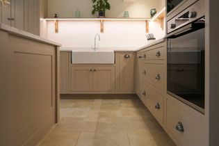 Warm, minimalist kitchen with beige cabinetry, farmhouse sink, and modern appliances. Open shelves display plants and jars, creating a cozy atmosphere.