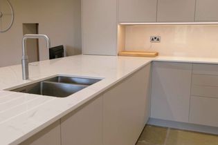 Modern kitchen with a sleek white counter, stainless steel sink, and minimalist cabinetry. A chopping board near a tiled backsplash, creating a clean look.