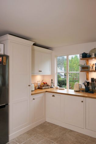 Bright kitchen with white cabinets, wooden countertops, and utensils. A window shows greenery outside, creating a inviting atmosphere.