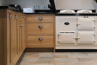 Warm shaker kitchen featuring wooden cabinets with metallic handles, a classic cream-colored stove with multiple compartments, and a tiled floor.