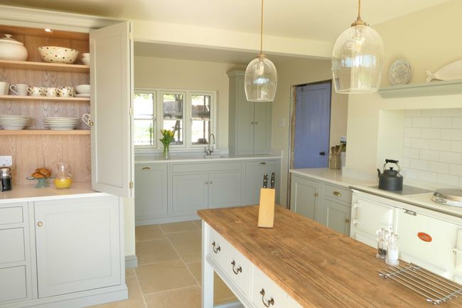 Bright shaker kitchen with cream cabinets, wooden island, and pendant lights. Open shelves display dishes, and a vase of tulips sits by the window. Cozy and inviting.