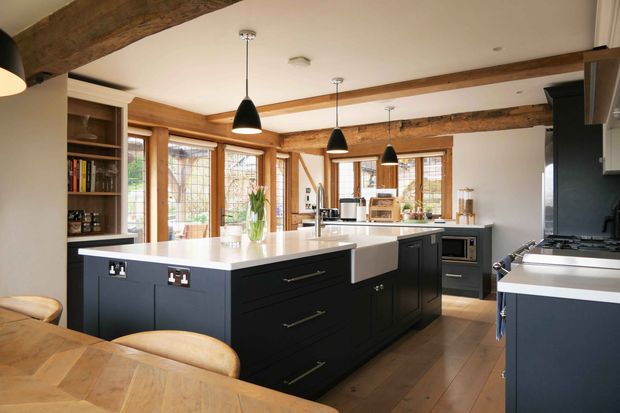 Bright Shaker kitchen with dark cabinetry, white islands, exposed wooden beams, large windows, and three pendant lights.