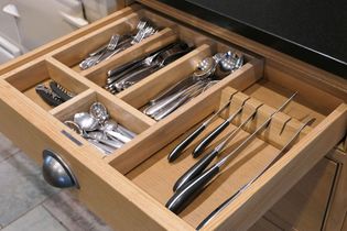 Open wooden drawer with neatly organised cutlery with forks, spoons, and knives in compartments. A corkscrew and small spoons also visible, conveying tidiness.