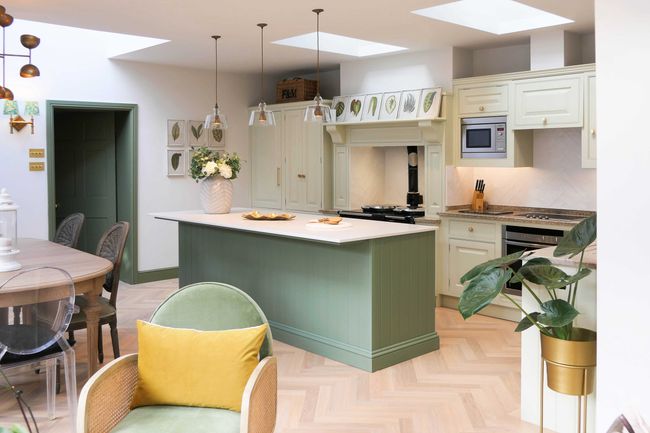 Elegant kitchen with soft green cabinetry, white quartz island, and pendant lights. Natural light highlights plants, creating a fresh, inviting atmosphere.