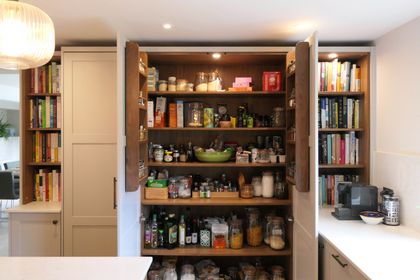 Walnut-lined larder with bi-fold doors open to fully stocked pantry shelves and door spice racks
