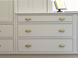 Light grey kitchen cabinets with brass handles and a white countertop. A recipe book on a stand is partially visible in the background.