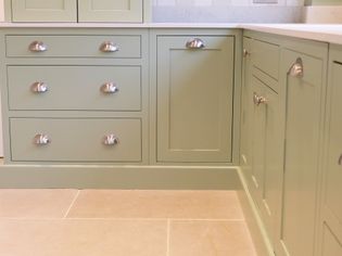 Green kitchen cabinets with silver handles, featuring drawers and cupboard doors. The light stone floor adds a clean, modern touch to the space.