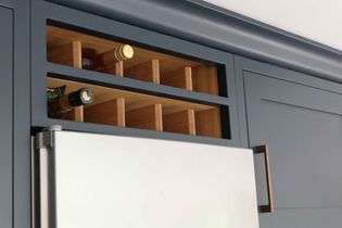 A blue kitchen cabinet with a wooden wine rack above, holding two bottles. The cabinet door features a sleek wooden handle, creating an elegant and modern look.