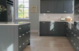 Shaker kitchen with dark grey cabinets, stainless steel handles, and light beige tile flooring. A large window lets in sunlight, creating a warm, inviting atmosphere.