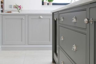 Shaker kitchen with grey cabinetry and silver handles. A vase with pink flowers and green plants sits on the white countertop, creating a fresh ambiance.