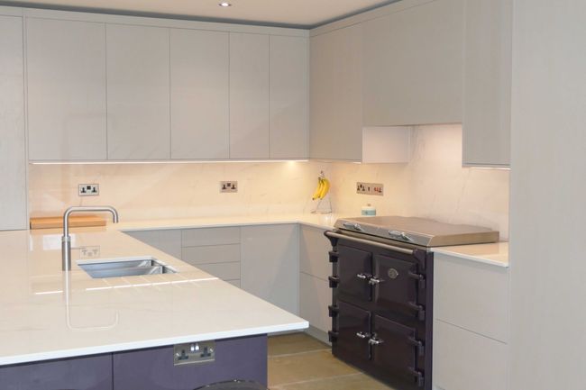 Modern kitchen with sleek, light-colored cabinets, a dark purple stove, and a spacious countertop with built-in sink