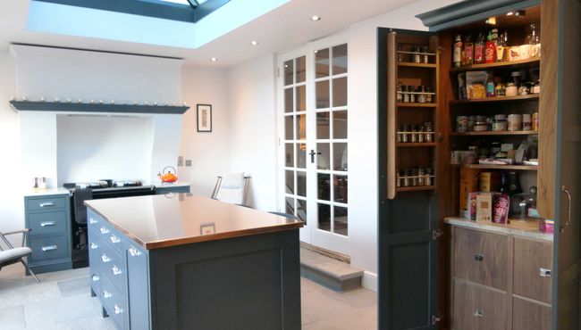 Shaker kitchen with a sleek central island, deep blue cabinetry, and a pantry stocked with spices and condiments; bright and organized ambiance.