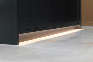 Under-cabinet lighting in a shaker kitchen highlights sleek black cabinetry and a light tiled floor, creating an elegant, minimalist ambiance.