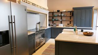 Sleek shaker kitchen with dark cabinets, stainless steel appliances, open shelving with dishes, and a colorful rug, conveying elegance.