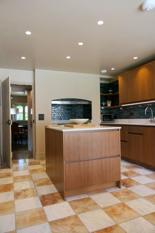 Modern kitchen with a wood island, dark tiled backsplash, white bowl, and cream-and-terracotta checkerboard floor.