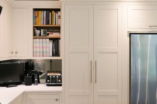 Cosy kitchen with white cabinets, filled shelves with books. A sleek toaster and TV sit on the counter, next to a stainless fridge.