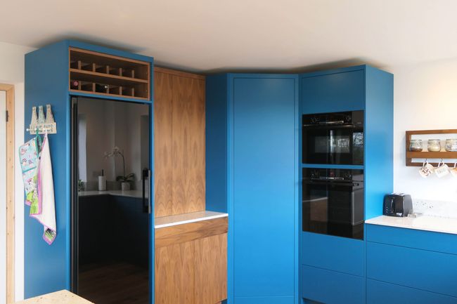 Bright blue modern kitchen with integrated fridge and oven, displaying a walk-in pantry door that blends into the perimeter cabinetry.