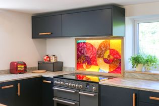 Navy blue modern kitchen located in ross-on-wye with red and yellow patterned splashback behind large range oven.