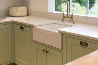 Shaker kitchen corner with pastel green cabinets, a white farmhouse sink, brass vintage-style tap, quartz countertop, and retro toaster.