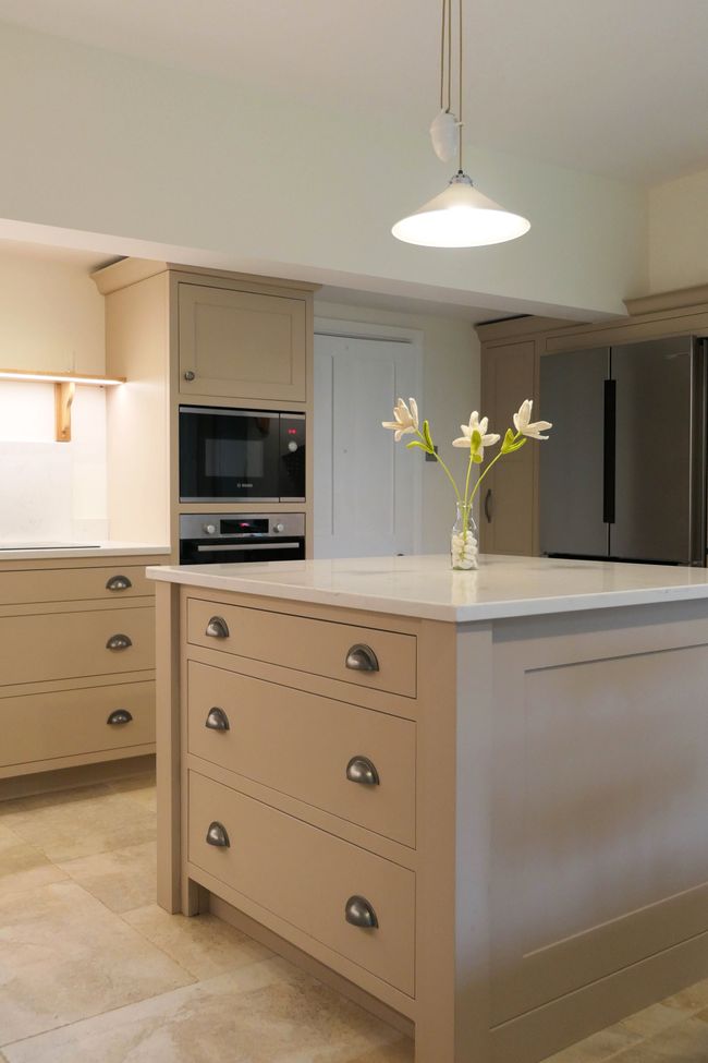 Shaker kitchen with beige cabinets, white countertops, and a central island with tulips in a vase. Pendant light above, stainless steel appliances.