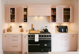 Pink cabinetry with four cupboards open displaying different items. Oven central of the image with an air fryer to the right.