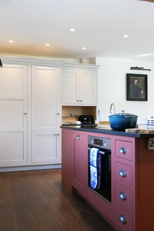 Shaker kitchen with white cabinets, burgundy island cabinetry, a blue pot on the counter, and a framed portrait on the wall.
