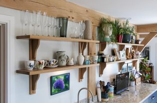 Shaker kitchen with blue cabinets and a marble countertop. Wooden shelves display plants, framed pictures, and ceramics. Bright, fresh, and organized ambiance.