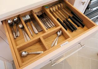 Open wooden cutlery drawer displaying neatly organised kitchen utensils.