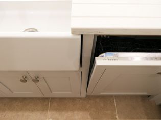 Farmhouse sink beside an open dishwasher with a light grey cabinet door. Neutral beige tile floor adds warmth to the functional kitchen scene.