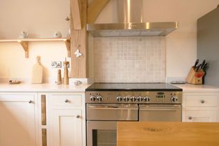 Shaker kitchen with stainless steel oven and range hood, white cabinets, and a wooden shelf holding decor.