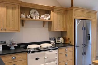 Warm kitchen with wooden cabinets, silver fridge, and cream-coloured stove. Above, shelves display charming polka dot crockery.