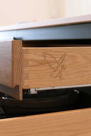 Open wooden drawer with dovetail joints showing an etched owl design on the side. The drawer is part of a smooth and modern kitchen setup.