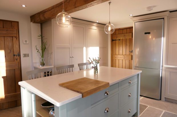 A neutral Shaker kitchen with a large island and white worktop, an exposed beam above and pendant lighting. 