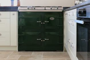 Green vintage oven with double doors, with white cabinets on a beige tiled floor in a kitchen setting.