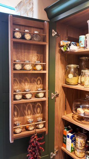 Open pantry cupboard with a spice rack on the inside of the door, various jars of baking ingredients on the shelves.