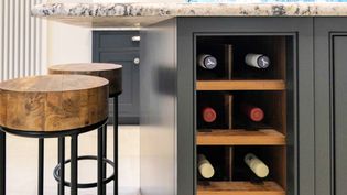 A shaker kitchen island with a granite countertop, featuring two wooden stools and a built-in wine rack holding six bottles horizontally.
