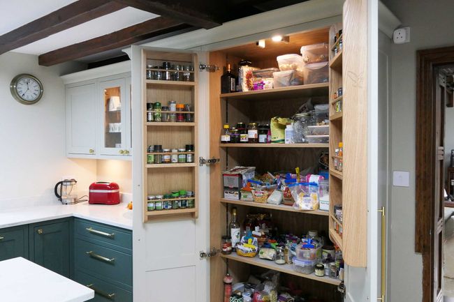 A well-organized pantry with open doors reveals shelves filled with jars, spices, and food items. A red toaster and mixer sit on a nearby counter.