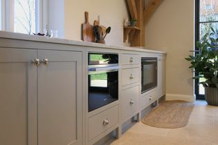 Shaker kitchen with neutral cabinets, built-in oven, and microwave. Wooden accents, a potted plant, and natural light create a calm ambiance.