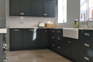 Shaker kitchen with dark grey cabinets, light countertops, and a farmhouse sink. A basket and toaster sit on the counter under soft natural light.