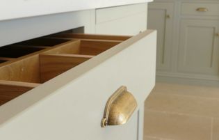 Open kitchen drawer with organized wooden dividers, set in cream coloured cabinetry. A brass handle enhances the elegant, minimalist design.