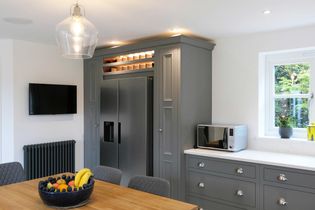 Shaker kitchen with grey cabinets, a stainless steel fridge, and a microwave on the counter. A fruit bowl sits on a wooden table nearby.