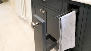 A shaker style pull out dark grey towel rail cabinet with silver nickel knobs.