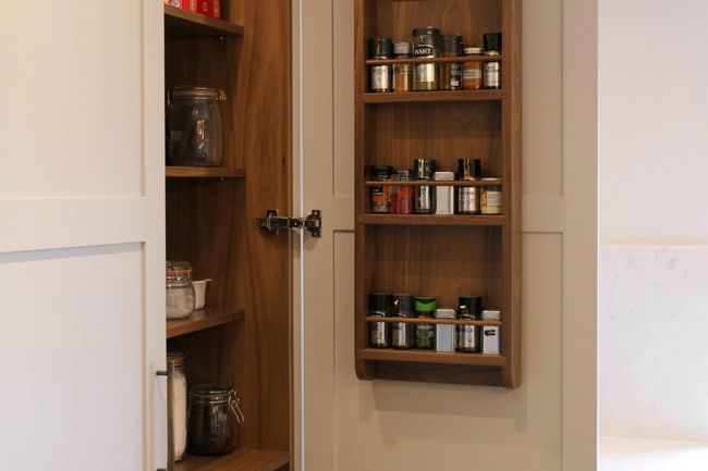 Open pantry door displaying a spice rack filled with various jars and containers. Sleek wood design creates a warm, organized kitchen atmosphere.