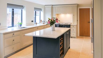 Shaker kitchen with cream cabinets, a dark blue island topped by a vase of colourful flowers, and windows overlooking a brick wall.