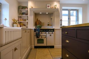 Traditional Shaker kitchen with cream cabinetry, a range cooker, open shelving, brass hardware, and a large dark wood island.