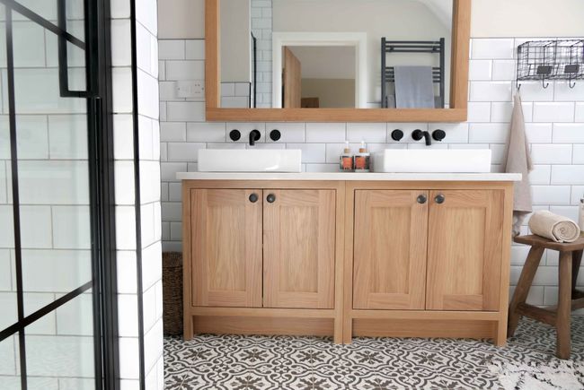 Bright bathroom with double sinks on a wooden vanity, black taps, and a large mirror. Patterned floor tiles and wall tiles add modern flair.