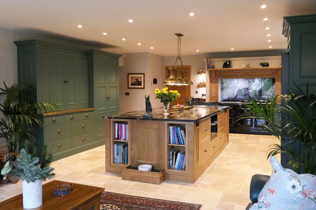 Warmly lit kitchen with dark green cabinets, a wooden island topped with yellow flowers.