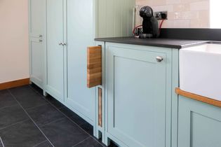 Shaker kitchen with light blue cabinets and black countertop. A pull-out chopping board is visible. A coffee machine sits on the counter next to a white sink.